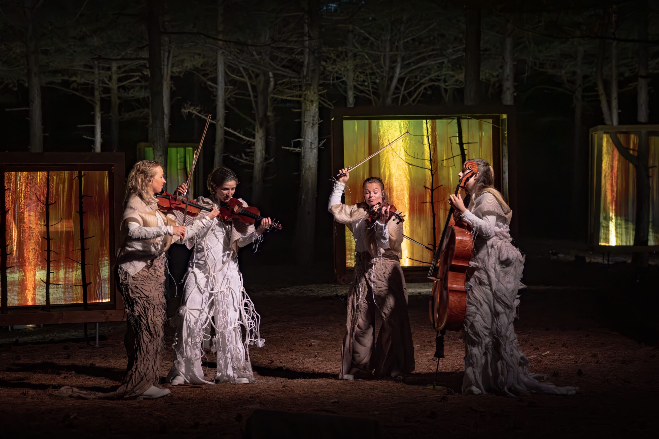 Ragazze Quartet in artistic clothing playing dynamically in a dark forest